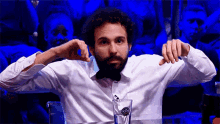 a man with a beard wearing a bow tie is sitting at a table with a glass of water in front of him