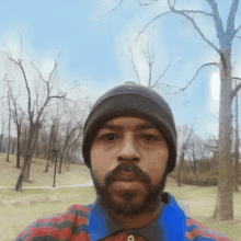 a man with a beard wearing a beanie and striped shirt takes a selfie in a park