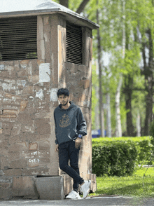 a man leans against a stone wall with graffiti on it that says ' 3 ' on it