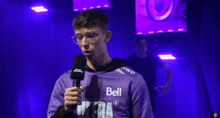 a man in a purple shirt that says bell on it is holding a microphone