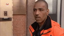 a man in an orange jacket is standing in front of a brick building with a sign that says ' amsterdam ' on it