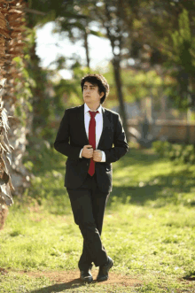 a man in a black suit and red tie is walking in the grass