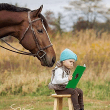 a little girl reading a book next to a horse