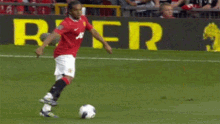 a man in a red jersey kicking a soccer ball on a field with a beer sign in the background