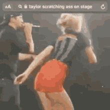 a man is singing into a microphone next to a woman in red shorts on stage .