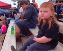 a young boy with long hair is sitting on a bench in a stadium .