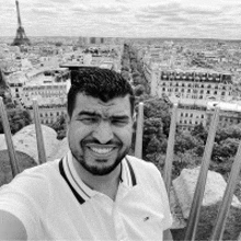 a man with a beard is taking a selfie with the eiffel tower in the background .