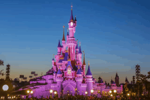 the disney castle is lit up in pink and blue