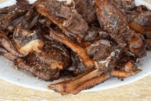 a white plate topped with a pile of fried meat on a wooden table .