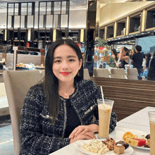 a woman sits at a table with a plate of food and a drink in front of her