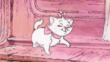 a white cat with a pink bow around its neck is walking on a pink floor .