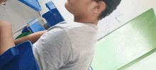 a boy sits at a desk in a classroom with a green board that says " a " on it