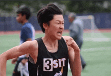 a young boy is running on a track and wearing a black tank top with the number 3 on it .