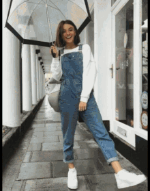 a woman in overalls is holding an umbrella in front of a store with the number 115 on the door