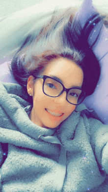 a woman wearing glasses and a gray hoodie is smiling