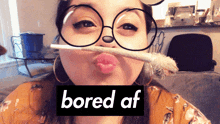 a woman wearing glasses has a cigarette sticking out of her mouth and the word bored af is behind her