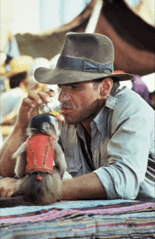 a man in a cowboy hat is drinking from a glass while a small monkey sits next to him