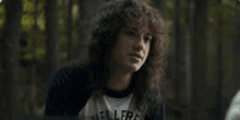 a woman with curly hair is sitting in the woods looking at the camera .