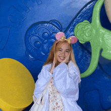 a woman wearing pink minnie mouse ears is standing in front of a blue wall with the number 80 on it