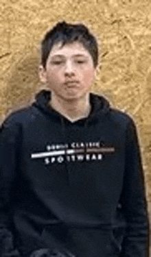 a young man is wearing a black hoodie and standing in front of a wooden wall .