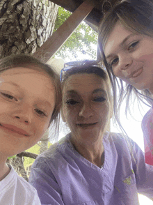 a woman wearing a purple shirt with a butterfly on the pocket smiles with two young girls