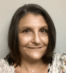 a woman with dark hair and a necklace smiles for the camera