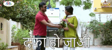 a man in a red shirt is giving flowers to a woman in a green dress in front of a sign that says adb