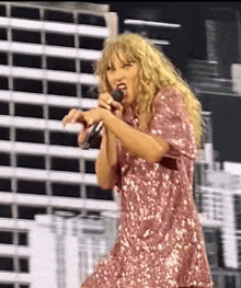 a woman in a pink sequined dress is singing into a microphone on a stage .