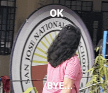 a woman in a pink shirt is standing in front of a sign that says ok bye