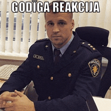 a man in a police uniform is sitting at a desk with his hands folded in front of him .