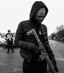 a man in a hooded jacket is holding a gun and wearing glasses and a bandana on his head