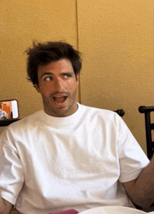 a man wearing a white t-shirt is sitting at a table with his mouth open