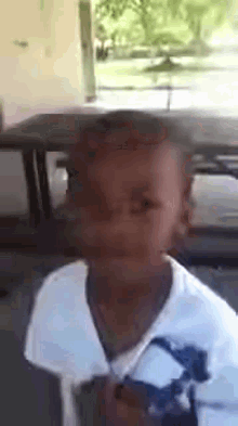 a young boy in a white shirt is standing in front of a car .