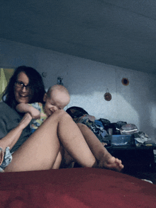 a woman sits on a bed holding a baby on her lap