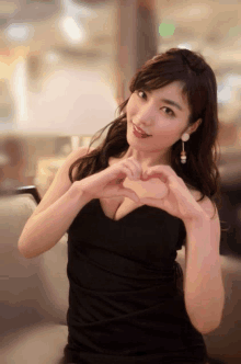 a woman in a black dress is making a heart with her hands