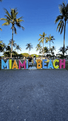 a group of people standing in front of a colorful sign that says miami beach