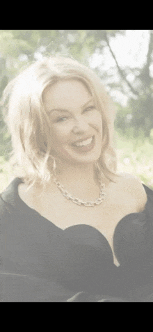 a woman is wearing a black dress and a necklace and smiling .