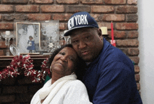 a man wearing a new york hat is hugging his wife