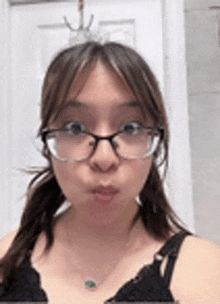 a young woman wearing glasses and a black tank top is making a funny face .