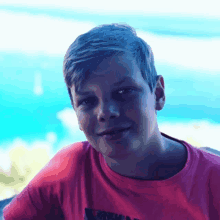 a young boy wearing a red t-shirt looks at the camera with the ocean in the background