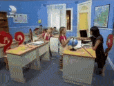 a group of children are sitting at desks in a classroom with a woman standing in front of them holding a globe .