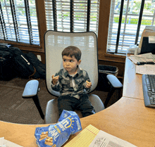 a young boy sits in an office chair eating a bag of mrs. chips