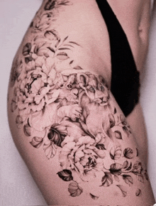 a woman has a tattoo of two lion cubs surrounded by flowers on her thigh