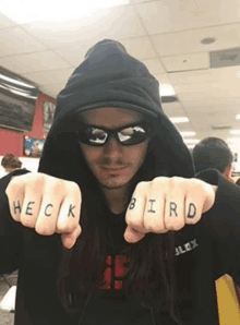 a man with long hair is wearing a hoodie and sunglasses and has the word bird tattooed on his fists .