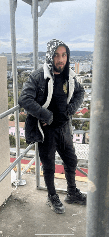 a man in a black jacket and black pants stands on a balcony overlooking a city