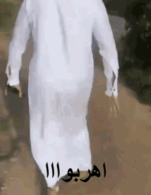 a man in a white robe is walking down a dirt road