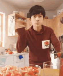 a young man in a red sweatshirt is standing in a kitchen with a bowl of strawberries on the counter .