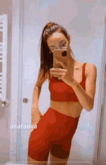 a woman in a red crop top and shorts is taking a selfie in the mirror .