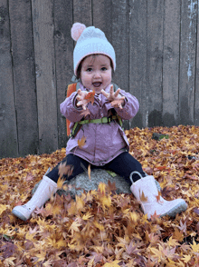 a little girl is sitting in a pile of leaves and holding a leaf