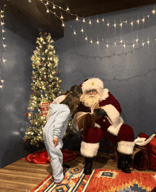 a little girl standing next to a santa reading a book